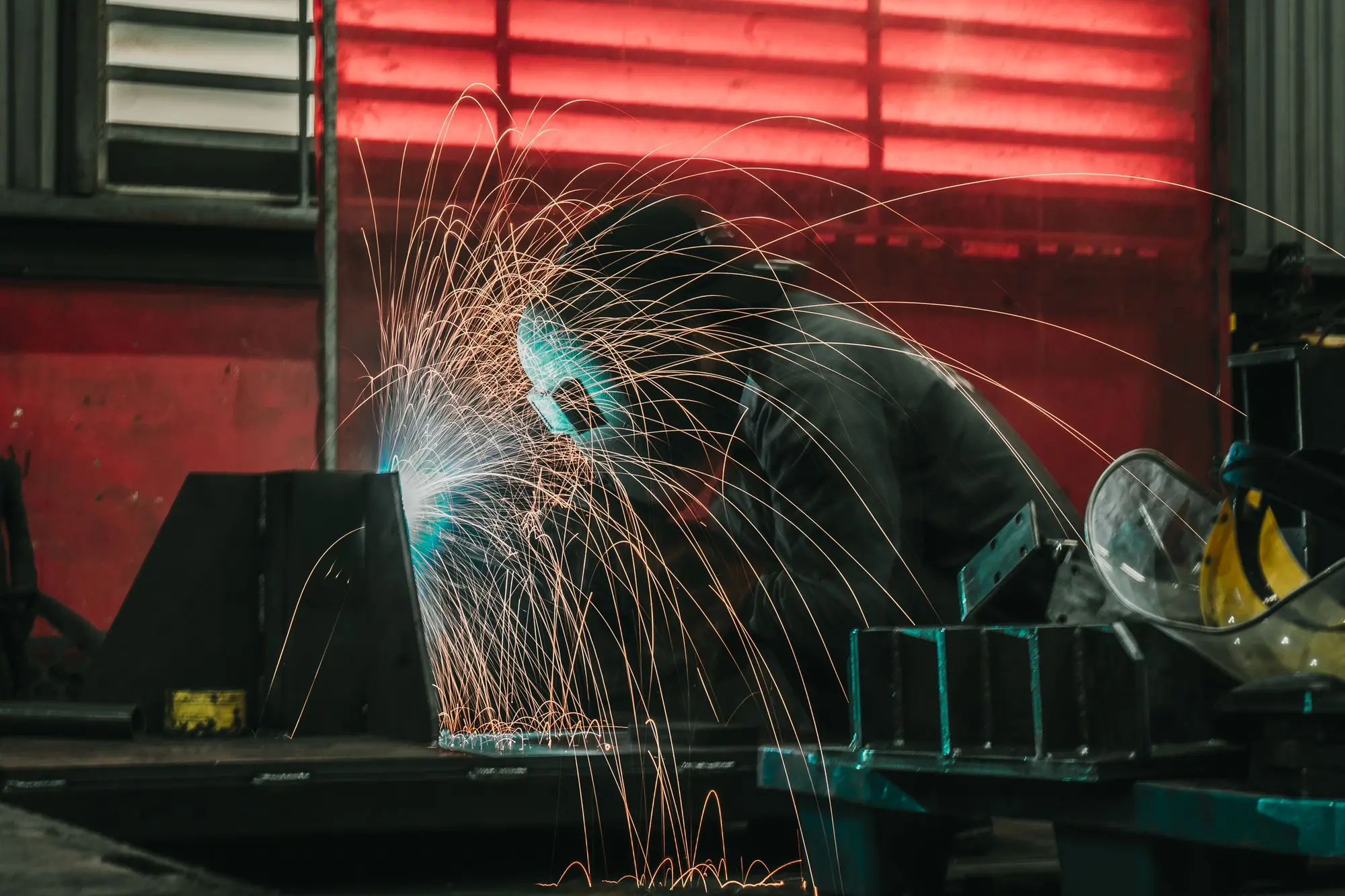 A welder working on a steel piece, sparks arcing across a dark workshop.